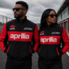 Black couple wearing black and red Aprilia SR50 racing bomber jackets standing on a racetrack, showcasing premium embroidered motorsport apparel.