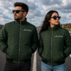 Man and woman wearing green Aston Martin bomber jackets standing on a highway, showcasing premium embroidered luxury motorsport apparel.